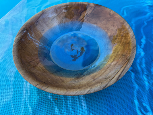 view of a mermaid and two babies swimming inside of a wood nut bowl